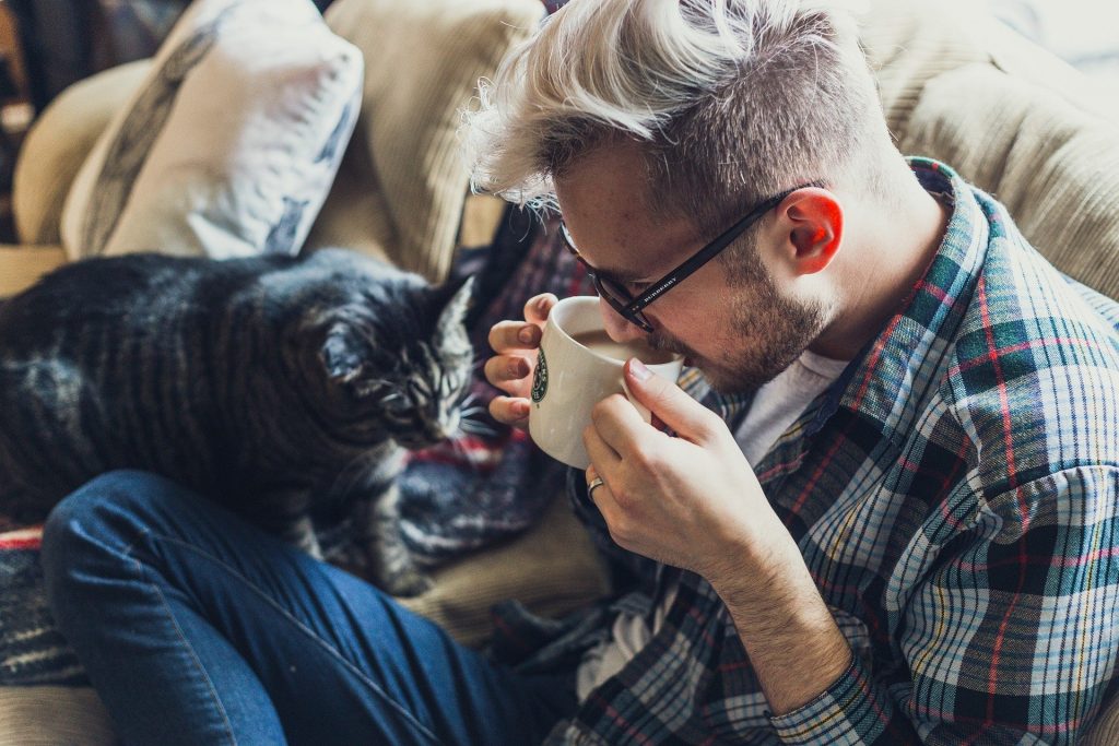 Man sipping coffee on sofa with cat