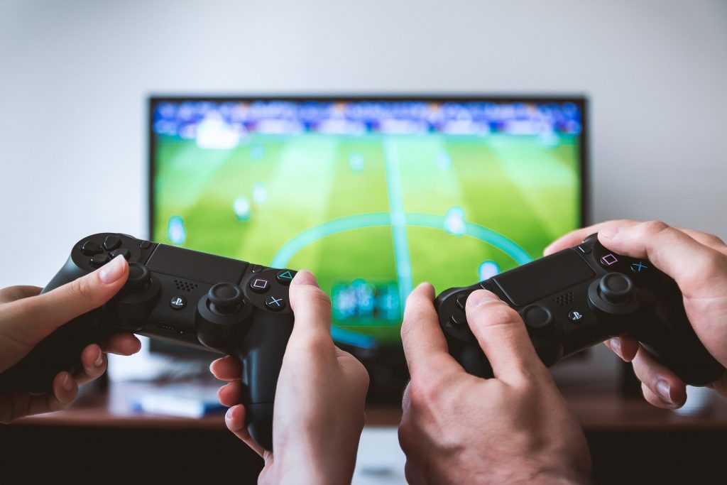 Two pairs of hands playing football video game on TV