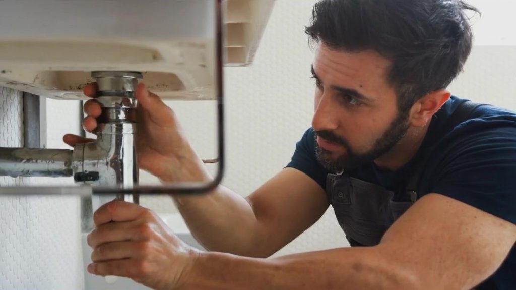 Man fixing pipes underneath sink