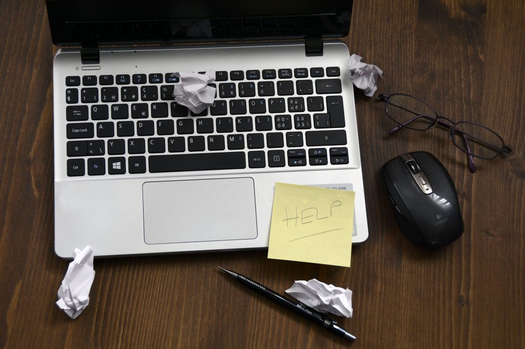 Laptop with balled up pieces of paper and note saying 'HELP'
