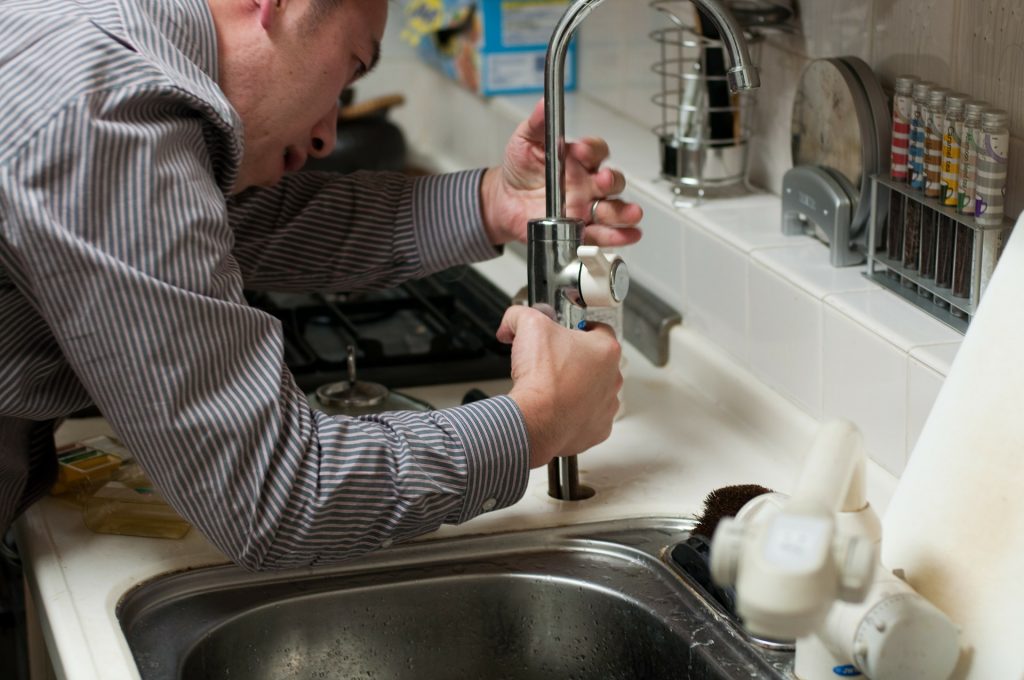 Man in shirt fixing a kitchen tap